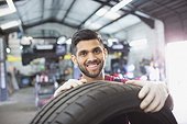 Portrait confident male mechanic with tire in auto repair shop