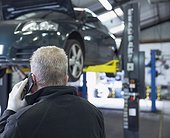 Male mechanic talking on smart phone in auto repair shop
