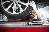 Portrait confident, smiling male mechanic working under car in auto repair shop