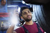 Focused male mechanic with flashlight examining tire in auto repair shop