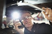 Male mechanic with flashlight working under car in auto repair shop