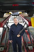 Portrait confident male mechanic under car in auto repair shop
