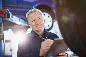 Smiling male mechanic with clipboard working in auto repair shop