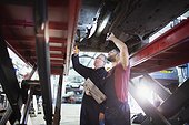 Male mechanics with flashlight working under car in auto repair shop