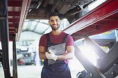 Portrait confident male mechanic with clipboard working under car in auto repair shop