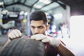 Focused male mechanic examining tire in auto repair shop
