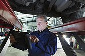 Male mechanic using diagnostic equipment under car in auto repair shop