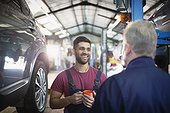 Smiling, happy male mechanics talking and drinking coffee in auto repair shop