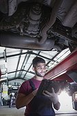 Male mechanic using diagnostic equipment under car in auto repair shop