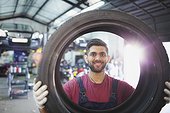 Portrait confident, smiling male mechanic holding tire in auto repair shop