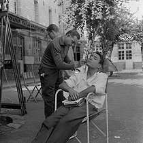 Roger-Viollet | 540380 | Shooting of  La Verte Moisson , film by François Villiers (1959). Claude Brasseur and a make-up artist. France, 1959. | © Alain Adler / Roger-Viollet