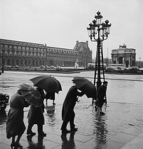 Roger-Viollet | 706915 | Passers-by in front of the triumphal arch of the Carrousel and the Louvre museum. Paris (Ist arrondissement), 1955. Photograph by Janine Niepce (1921-2007). | © Janine Niepce / Roger-Viollet