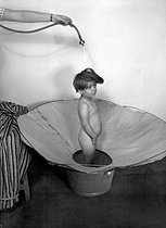 Roger-Viollet | 831116 | Child having a shower. Cloth device replacing the tub, 1946. | © Jacques Boyer / Roger-Viollet