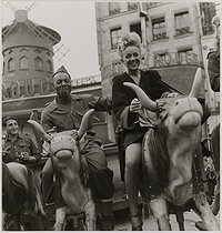 Roger-Viollet | 832669 | Young woman and US soldiers on a merry-go-round in front of the Moulin Rouge, place Blanche. Paris (IXth arrondissement), 1945. Photograph by Roger Schall (1904-1995). Paris, musée Carnavalet. | © Roger Schall / Musée Carnavalet / Roger-Viollet